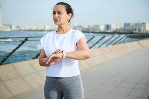 atletisk kvinna ser in i de distans, kontroll kondition Ansökan på smart klocka, få redo för morgon- jogga foto