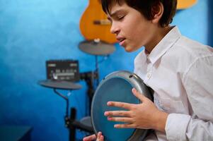 närbild porträtt tonåring pojke med ögon stängd, spelar de djembe trumma i en mysigt Hem musik studio, slår trummor, skapande de rytm av etnisk musik. äkta afrikansk percussion musikalisk instrument foto