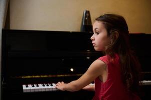 liten pianist musiker flicka spelar piano och sång låt, skapande musik, utför och komponera melodi på de pianoforte. skol är praktiserande på ackord instrument foto