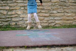 närbild av en sportig unge flicka spelar hoppa hage, tar vänder Hoppar över kvadrater markant på lekplats. foto