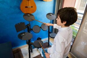 över huvudet se av en latinamerikan tonåring pojke musiker använder sig av trumpinnar, stryk på de trumma medan utför ljud, känsla de rytm av musik. trumma uppsättning - percussion musikalisk instrument. foto