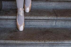 närbild av ballerinas pointes på de grå sten steg bakgrund. dansa Sammanträde på de steg. ballerina fötter med rosa balett tofflor på. minimalistisk, enkel. kopia Plats. foto