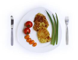 hemlagad friterad riven potatis pannkakor eras med färsk tomater och grön lök på de vit tallrik, gaffel och kniv. draniki. topp se. Skära ut och isolerat med klippning väg på de vit bakgrund foto