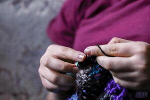 skicklig fingrar av en ung lady innehav virka krok och ull tråd. flickor händer virkning handgjort jacka. hantverk hobby, skapande unik kläder för kraft konst eller jordbrukare mode marknadsföra. foto