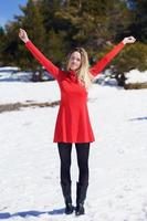kvinna som bär en röd klänning och svarta strumpor öppnar armarna av lycka i de snöiga bergen.