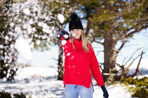 ung kvinna kastar snöbollar framåt i en snötäckt skog i bergen