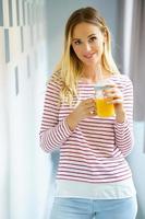 glad kvinna dricker ett glas naturlig apelsinjuice hemma.