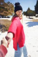 blond kvinna i vinterkläder går och håller sin partners hand i de snöiga bergen.