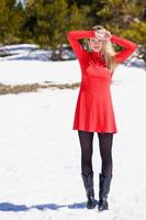 ung blond kvinna som bär en röd klänning och svarta strumpor i de snöiga bergen på vintern.