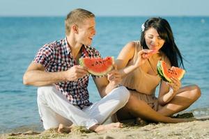 kille och en tjej på stranden äter en mogen vattenmelon foto