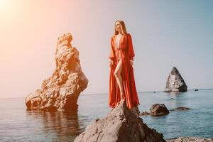 kvinna resa hav. ung Lycklig kvinna i en lång röd klänning Framställ på en strand nära de hav på bakgrund av vulkanisk stenar, tycka om i Island, delning resa äventyr resa foto