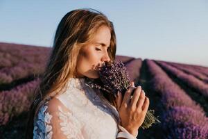 kvinna lavendel- fält. Lycklig sorglös kvinna i en vit klänning gående i en lavendel- fält och lukta en lavendel- bukett på solnedgång. idealisk för värma och inspirera begrepp i reslust och resa. foto