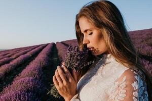 kvinna lavendel- fält. Lycklig sorglös kvinna i en vit klänning gående i en lavendel- fält och lukta en lavendel- bukett på solnedgång. idealisk för värma och inspirera begrepp i reslust och resa. foto