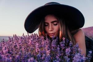 kvinna lavendel- fält. Lycklig sorglös kvinna i svart klänning och hatt med stor brätte lukta en blomning lavendel- på solnedgång. perfekt för inspirera och värma begrepp i resa och reslust. stänga upp foto