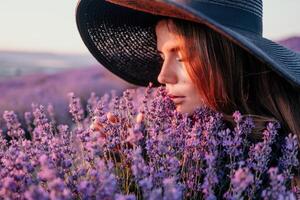 kvinna lavendel- fält. Lycklig sorglös kvinna i svart klänning och hatt med stor brätte lukta en blomning lavendel- på solnedgång. perfekt för inspirera och värma begrepp i resa och reslust. stänga upp foto