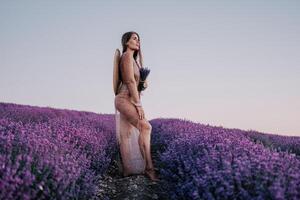 kvinna lavendel- fält. Lycklig sorglös kvinna i beige klänning och hatt med stor brätte lukta en blomning lavendel- på solnedgång. perfekt för inspirera och värma begrepp i resa och reslust. stänga upp foto