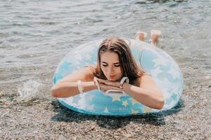 kvinna sommar hav. Lycklig kvinna simning med uppblåsbar munk på de strand i sommar solig dag, omgiven förbi vulkanisk berg. sommar semester begrepp. foto