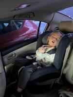 liten flicka sover i en bebis bil sittplats i de tillbaka sittplats av en bil med en plysch kanin foto