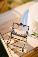 par av bröllop ringar lögner i en glas låda Nästa till en bröllop kaka på en trä- låda foto
