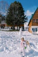 liten flicka med en kälke på en rep går ner de kulle över en snögubbe foto