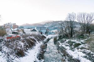 berg flod flöden mellan de snötäckt banker av en by på de fot av de bergen foto