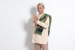 porträtt av attraktiv asiatisk muslim man i koko skjorta med bön matta som visar be om ursäkt och Välkommen hand gest. ursäkt under eid mubarak. isolerat bild på vit bakgrund foto