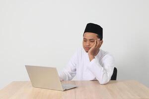 porträtt av trött asiatisk muslim man i koko skjorta med kalott arbetssätt under fasta på ramadan månad, känsla sömnig, gapande med hand beläggning mun. isolerat bild på vit bakgrund foto