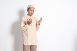 porträtt av religiös asiatisk muslim man i koko skjorta med kalott bön- ärligt med hans händer Uppfostrad. from tro begrepp. isolerat bild på vit bakgrund foto