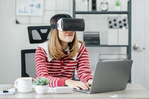 kvinna i en randig Tröja och virtuell verklighet headsetet sitter på en skrivbord med en bärbar dator, kaffe kopp, och växt. foto