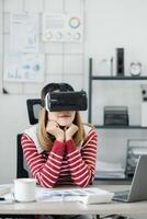 kontemplativ ung kvinna med en vr headsetet sitter på henne kontor arbetsyta, utforska virtuell miljöer. foto