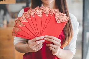 en närbild av en kvinna innehav en fläkt av utsmyckad röd kuvert, en traditionell symbol av tur och välstånd i asiatisk kulturer, ofta utbytt under särskild tillfällen. foto