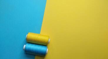 spolar av tråd och en nål på en gul och blå bakgrund, kontrast konsept foto