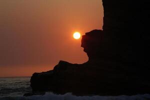 Sol nära solnedgång över hav och klippig klippa foto