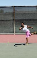leende svart kvinna svängande tennis racket på domstol foto