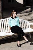 leende ung asiatisk amerikan kvinna Sammanträde på bänk utomhus foto
