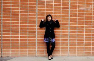 leende attraktiv asiatisk amerikan kvinna stående tegel vägg foto