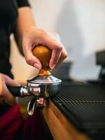 hand av en Barista innehav en portafilter och en kaffe manipulera framställning ett espresso kaffe. Barista trycker på jord kaffe använder sig av en manipulera i en kaffe affär foto