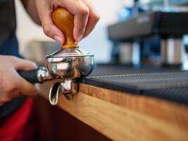 hand av en Barista innehav en portafilter och en kaffe manipulera framställning ett espresso kaffe. Barista trycker på jord kaffe använder sig av en manipulera i en kaffe affär foto