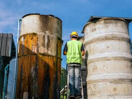 ingenjör kontrollerande de kvalitet av vatten stå på de riskabel trappa på hög platser rörelse industriell vatten rening eller filtrering Utrustning gammal cement tankar för förvaring vatten i vatten fabrik foto