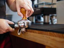 hand av en Barista innehav en portafilter och en kaffe manipulera framställning ett espresso kaffe. Barista trycker på jord kaffe använder sig av en manipulera i en kaffe affär foto