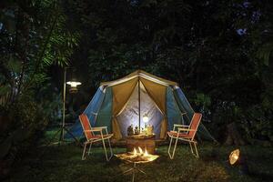 årgång stuga tält, antik olja lampa, retro stolar, grupp av camping tält med utomhus- kaffekokning anläggningar på trä- tabeller i en skog camping område i de skog. foto