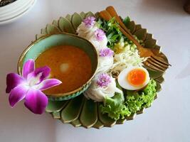 thai mat består av spaghetti och kokos mjölk curry och garnering de tallrik med kokt ägg, sallad och orkidéer foto