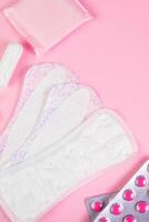 uppsättning av feminina hygienprodukter för menstruation. bindor, tamponger, piller på rosa bakgrund. foto