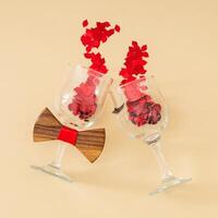 romantisk layout av vin glasögon, röd mun glitter konfetti, ögonfransar och rosett slips på beige bakgrund. människor livsstilar och relationer i kärlek begrepp. mode estetisk fest eller firande aning. foto