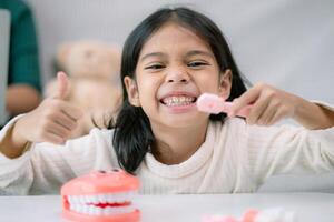 en ung flicka är leende och innehav en tandborste i främre av en leksak tandborste foto