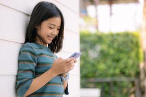 en ung flicka är leende medan ser på henne cell telefon foto