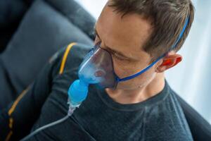 ohälsosam man bär nebulisator mask i Hem. hälsa, medicinsk Utrustning och människor begrepp. hög kvalitet Foto