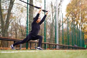 flicka idrottare Träning använder sig av trx på sportplats. blandad lopp ung vuxen kvinna do träna med suspension systemet. friska livsstil. stretching utomhus lekplats. foto