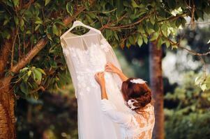 en skön brud står Nästa till en bröllop klänning med en budoar klädsel Nästa till en villa i italien.morgon av de brud i tuscany foto