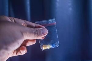 finger innehav tre piller för schizofrena inuti en plast klämma på en mörk bakgrund foto